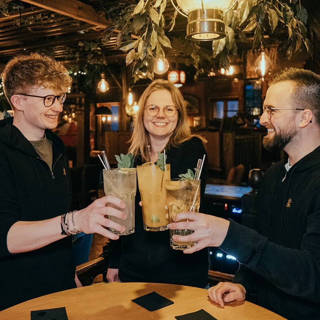 Drei Personen stoßen mit hohen Cocktailgläsern an