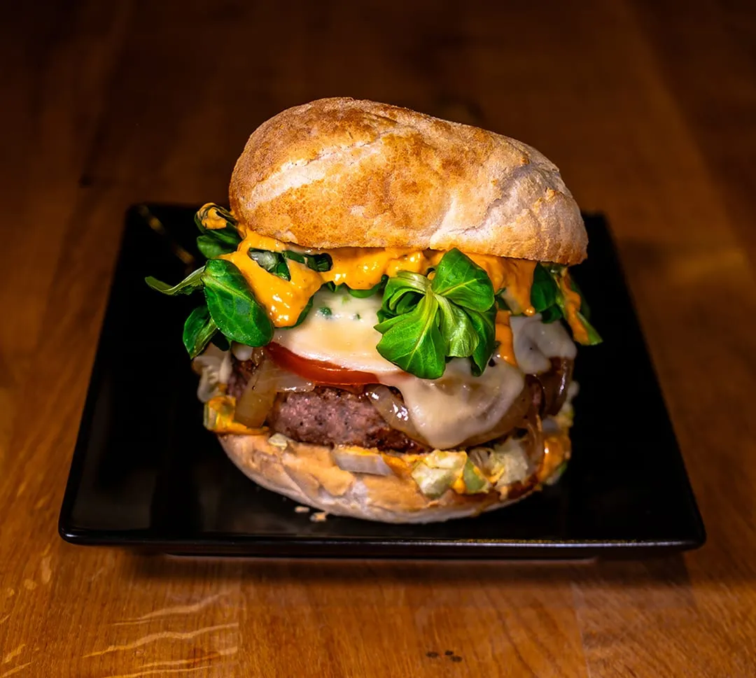 Burger mit Käse, Salat und Tomate auf einem schwarzen Teller