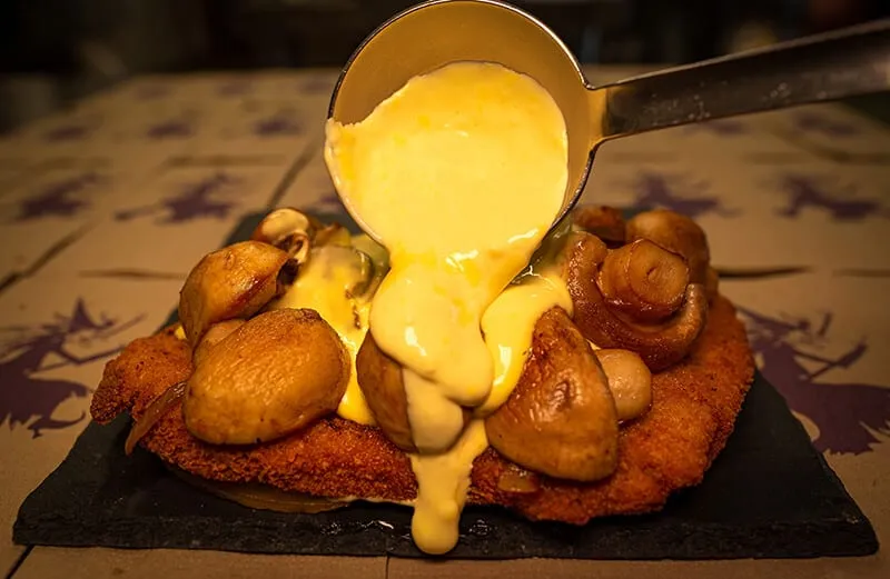 Sauce Hollandaise wird über ein paniertes Schnitzel mit Kartoffeln und Champignons gegossen