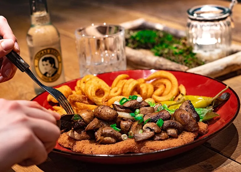Teller mit Zwiebelringen, Champignons und Frühlingszwiebeln auf einem panierten Schnitzel