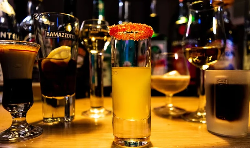 Ein gelber Shot mit rotem Zuckerrand steht auf dem Tresen, dahinter die Flaschenwand