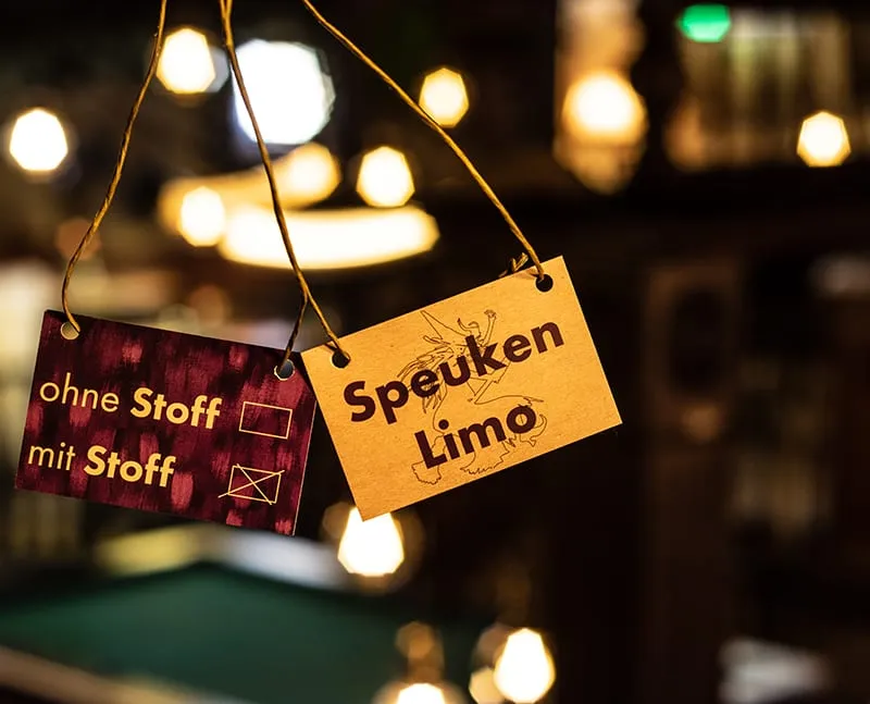 Holzschild mit der Aufschrift „Speuken Limo“ hängt vor Lichterketten